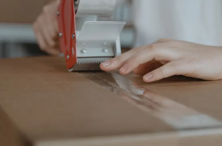 Hands sealing a cardboard carton with tape